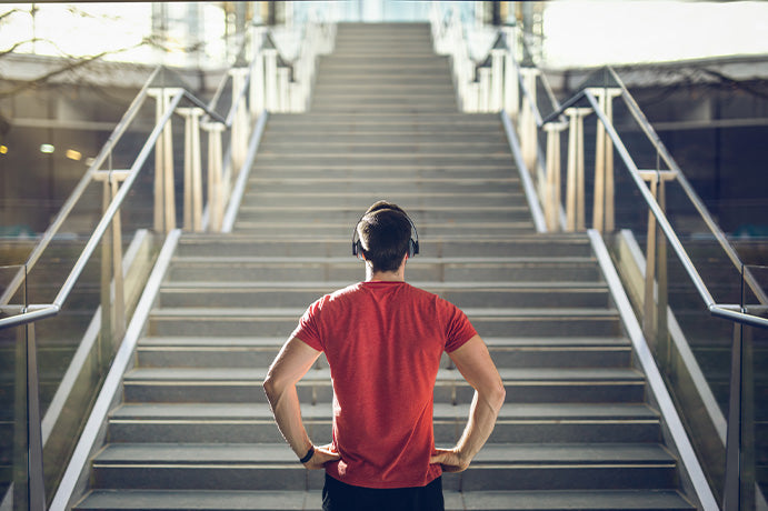 Kopfhörer tragender Mann in rotem T-Shirt steht vor einer Treppe um sie hoch zu laufen