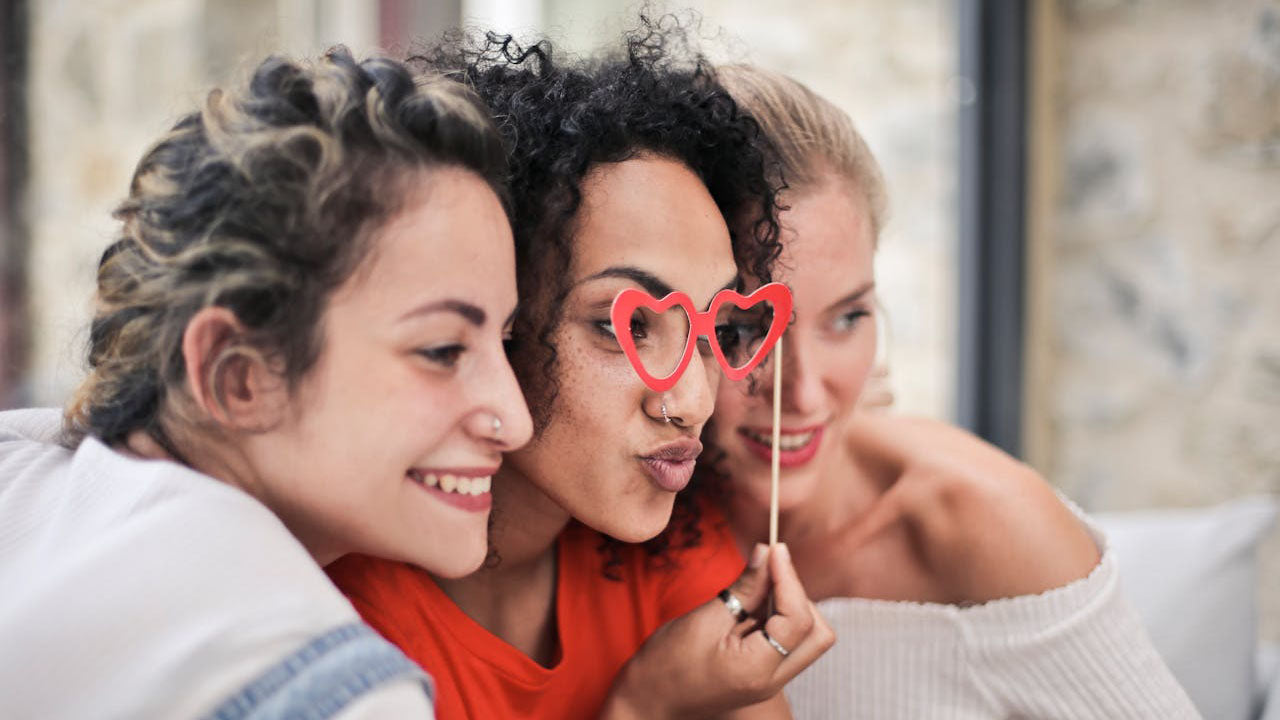 Drei Freundinnen in Profilansicht machen ein gemeinsames Foto mit roter Herzbrille