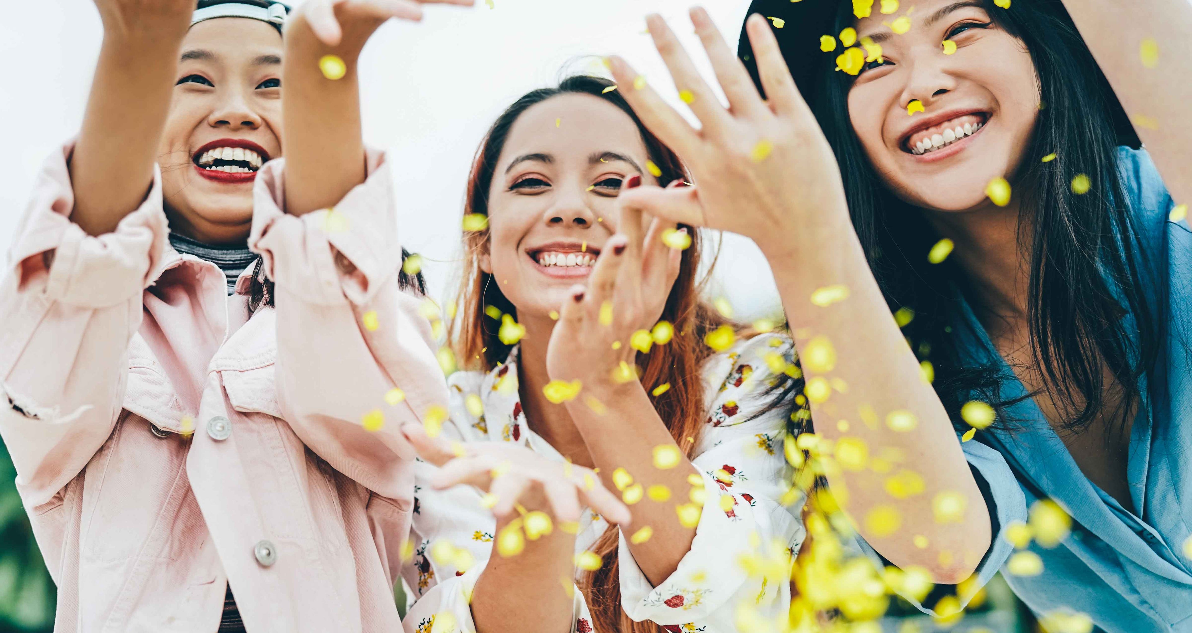 Drei fröhliche Frauen werfen gelbes Konfetti in die Luft