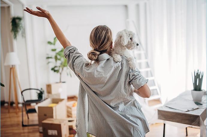 Frau steht mit Hund auf dem Arm in neuer Wohnung und freut sich