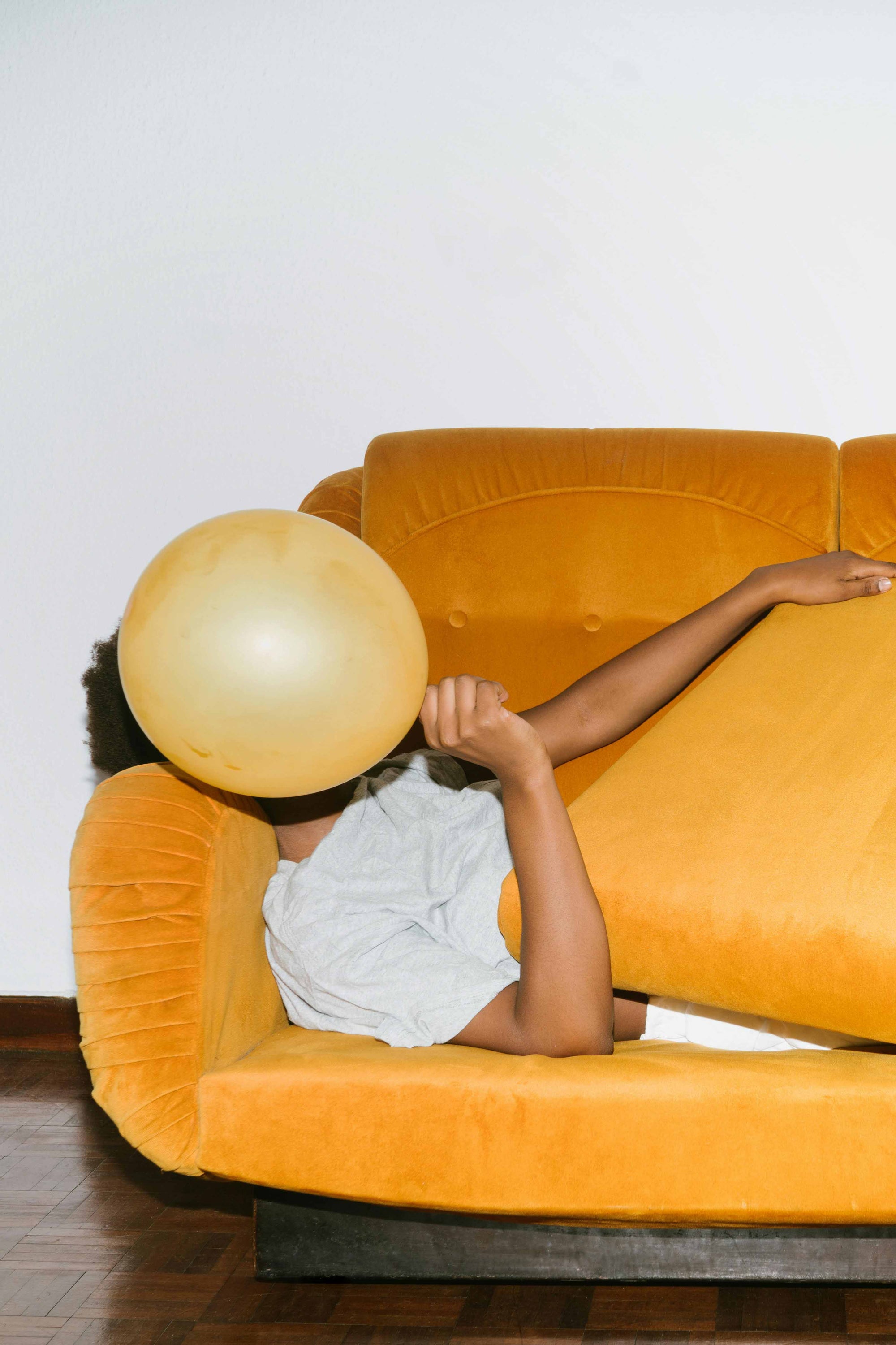 Frau liegt auf ockergelben Sofa und hält einen gelben Luftballon vor das Gesicht